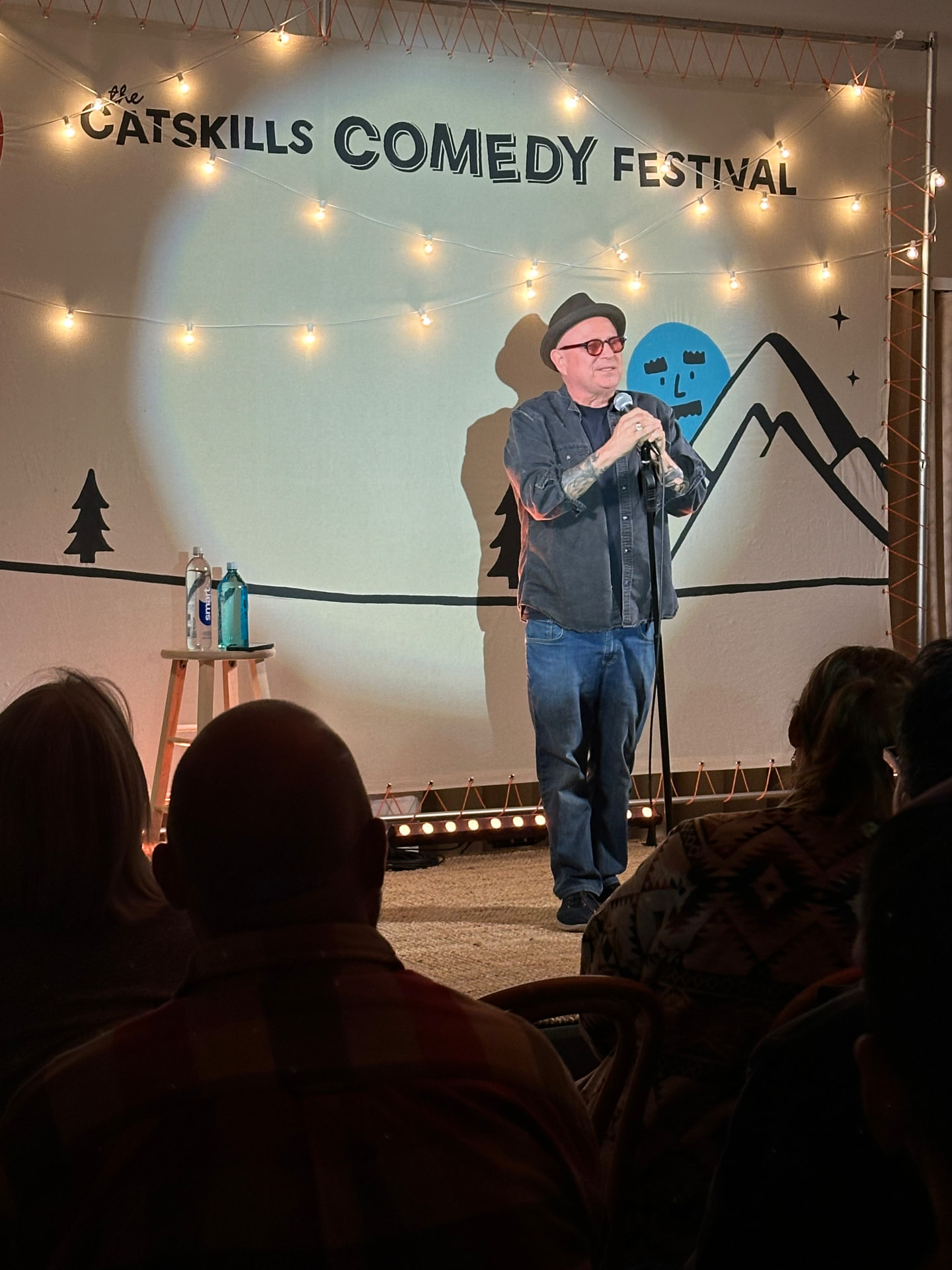 Comedian on the tent stage in front of the festival banner