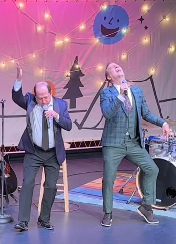 Two performers belting a song under the festival smiley banner